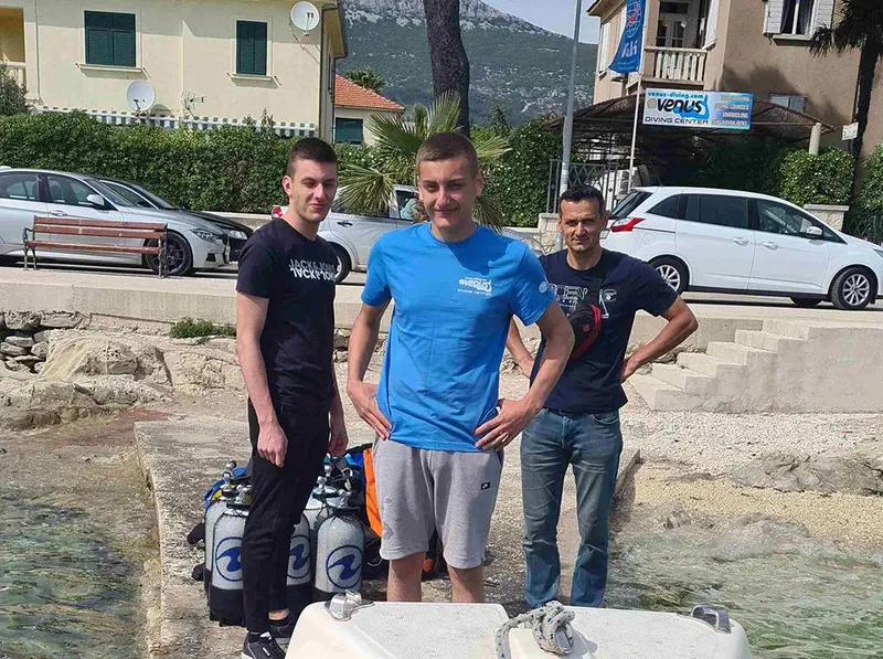 Trois plongeurs souriants avec bouteilles près du centre de plongée