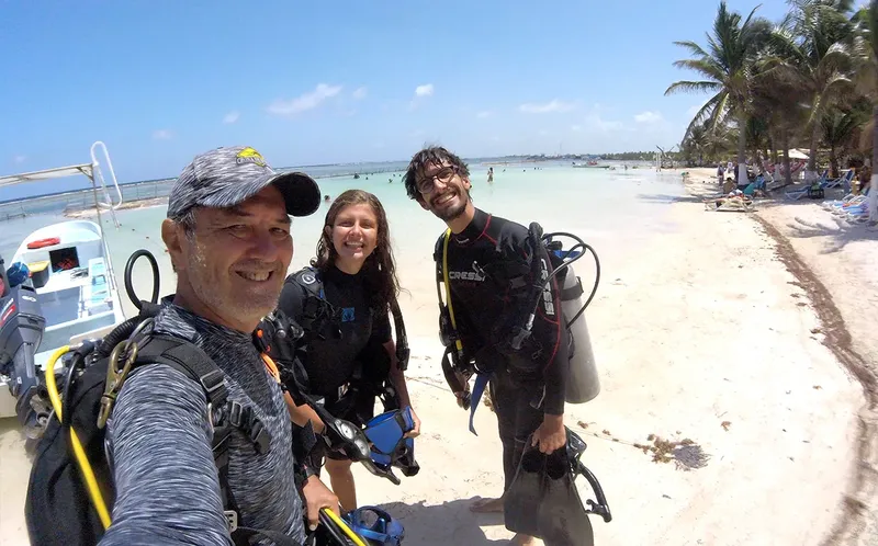 Trois plongeurs souriants équipés sur une plage tropicale ensoleillée