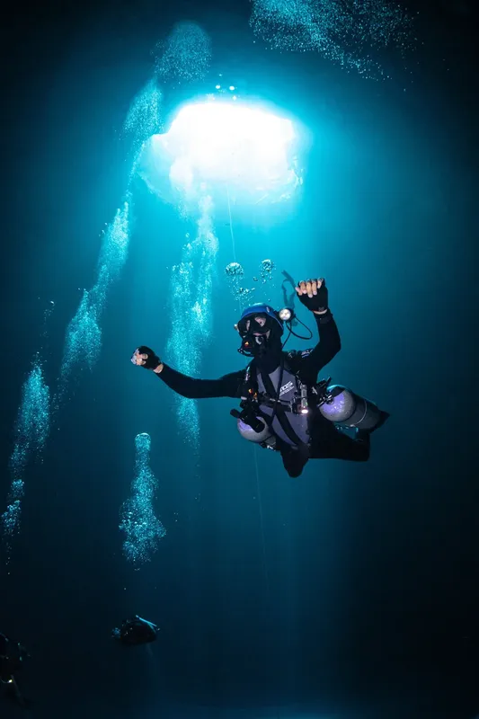 Plongeur en scaphandre, bras levés, dans une eau bleu profond éclairée