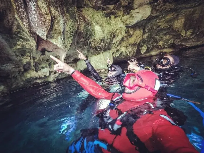Plongeurs explorent une grotte sous-marine, pointant vers une formation rocheuse