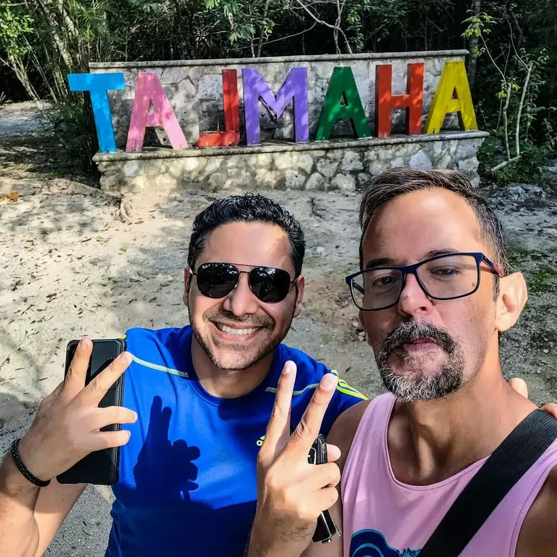 Deux hommes souriants devant une inscription colorée en extérieur