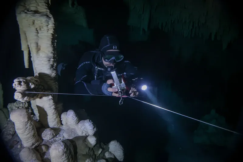 Plongeur en grotte sous-marine, éclairé par une lampe, suit un fil guide