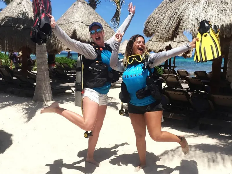 Deux femmes souriantes sur une plage, équipées pour la plongée
