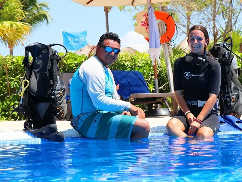 Deux plongeurs souriants équipés près d'une piscine ensoleillée