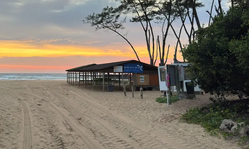Bâtiment bas sur plage de sable au coucher du soleil, enseigne visible