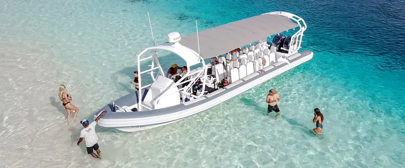 Bateau de plongée semi-rigide dans une eau turquoise avec des baigneurs