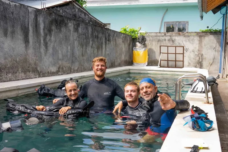 Quatre plongeurs souriants dans une piscine avec leur équipement complet