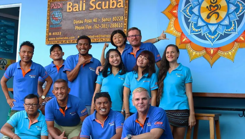 Groupe de personnes souriantes devant un mur bleu et une enseigne