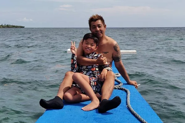 Deux personnes souriantes sur la proue d'un bateau bleu en mer