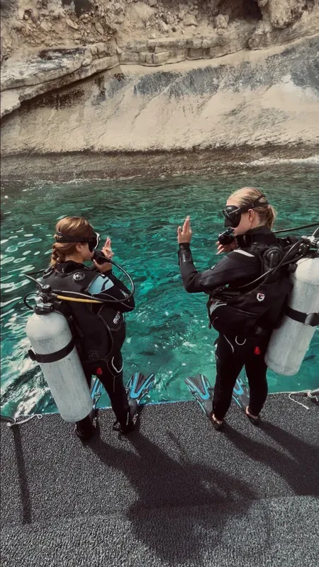 Deux plongeuses équipées se préparent à plonger en mer turquoise