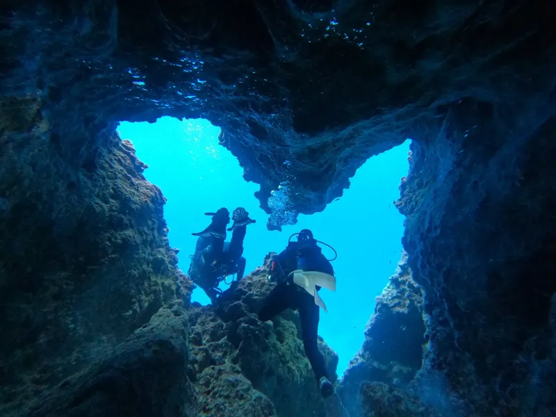 Deux plongeurs explorent une grotte sous-marine avec une lumière bleue