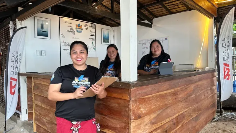 Trois femmes souriantes derrière un comptoir d'accueil ensoleillé