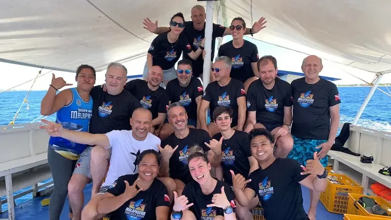 Groupe de plongeurs souriants sur un bateau en mer, faisant des signes