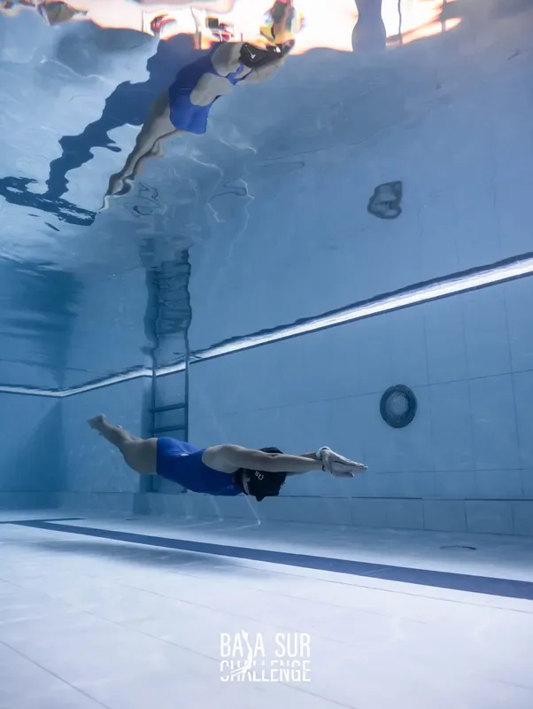 Deux plongeurs en apnée évoluent dans une piscine bleue claire