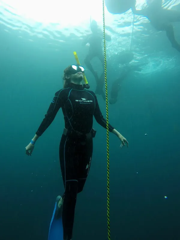 Plongeuse en combinaison flottant verticalement, tenant une corde jaune