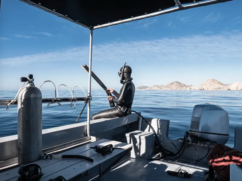 Plongeur en combinaison noire tenant une arme dans un bateau