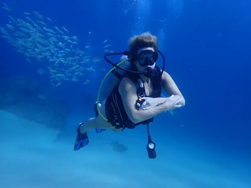 Plongeur en combinaison nageant dans une eau bleue claire avec des poissons