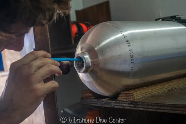 Technicien vérifiant l'étanchéité d'une bouteille de plongée avec un outil bleu