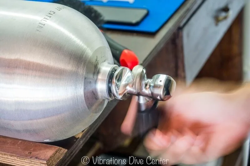 Une main manipule le robinet d'une bouteille de plongée en atelier