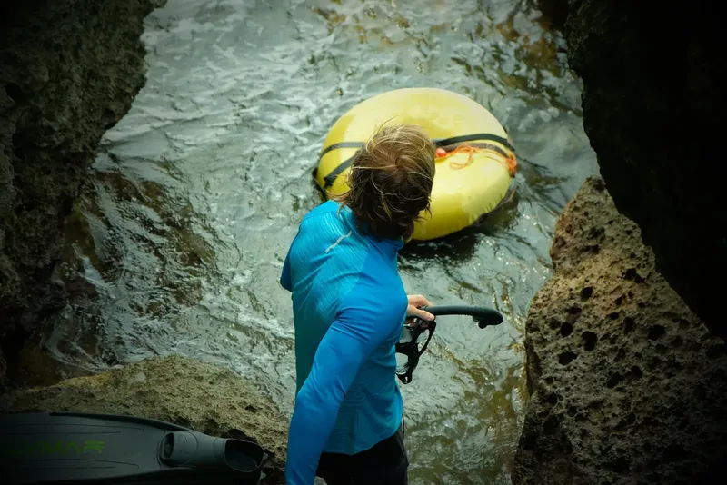 Plongeur entrant dans l'eau avec son matériel près des rochers