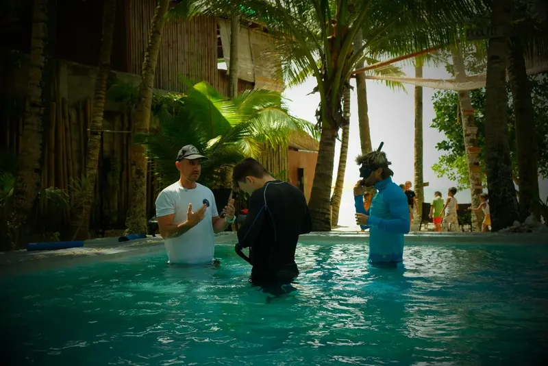 Trois personnes dans une piscine, un instructeur explique un équipement