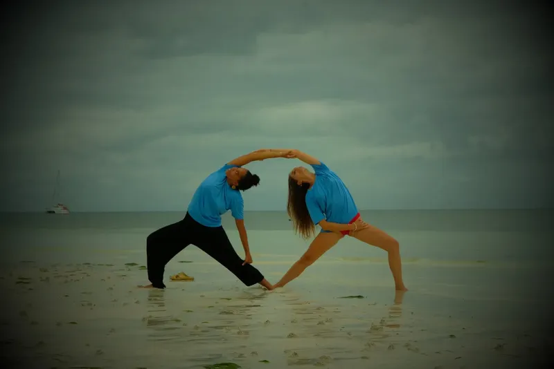 Deux personnes pratiquent une posture de yoga sur une plage