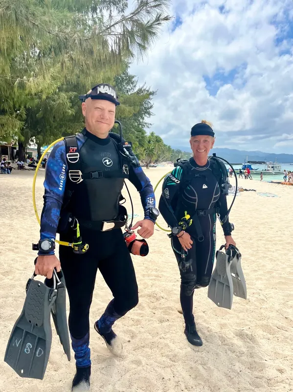 Deux plongeurs équipés marchent sur une plage ensoleillée vers la mer