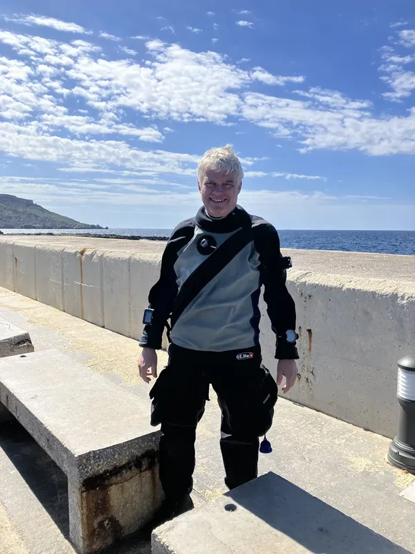 Plongeur souriant en combinaison complète sur un quai ensoleillé