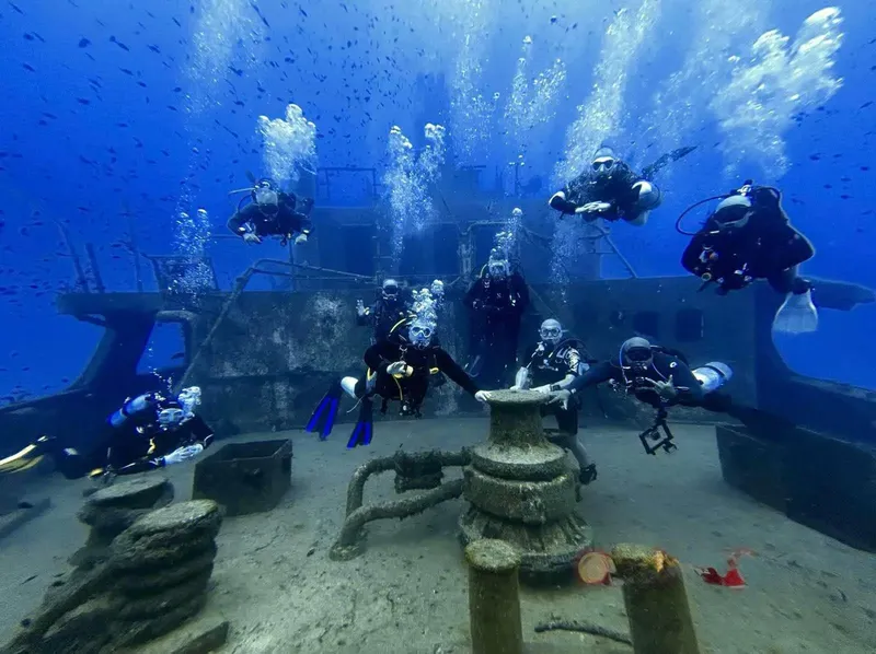 Groupe de plongeurs explorant l'épave d'un navire bleu et rouillé