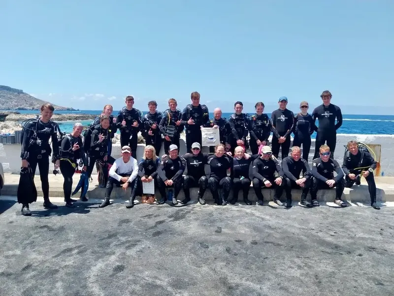 Groupe de plongeurs souriants posant ensemble sur un quai ensoleillé