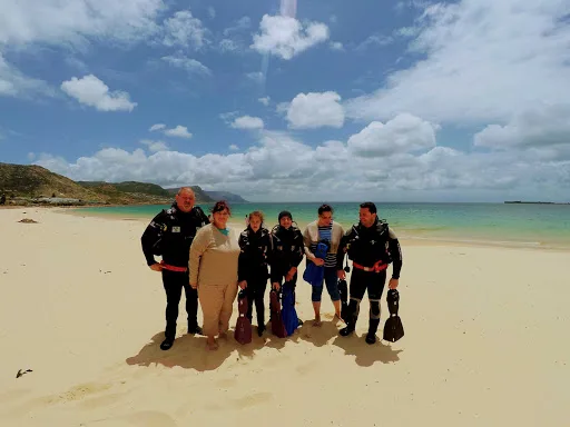 Groupe de plongeurs souriants sur une plage ensoleillée avec l'océan