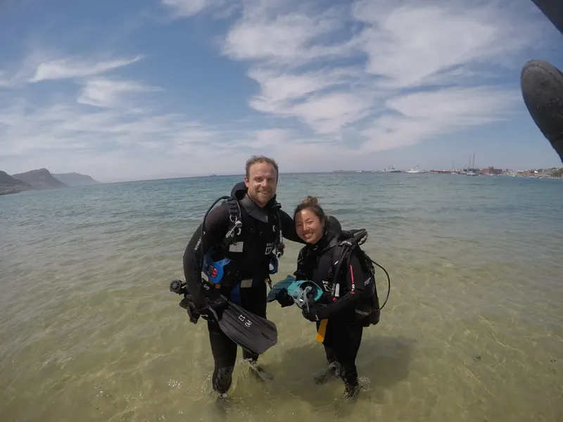 Deux plongeurs souriants en combinaison, équipés, dans l'eau turquoise