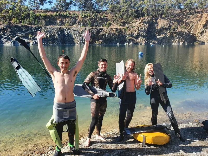 Quatre personnes souriantes en combinaison de plongée près d'un lac