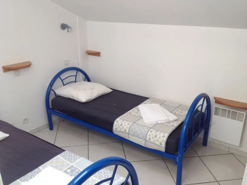 Chambre simple avec lits bleus, oreillers blancs et étagères murales