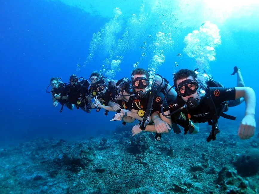 Groupe de plongeurs souriants en formation sous-marine, bulles et récif