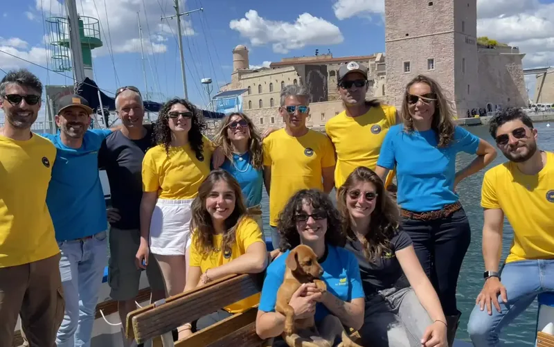 Groupe de personnes souriantes posant devant un bateau et un fort