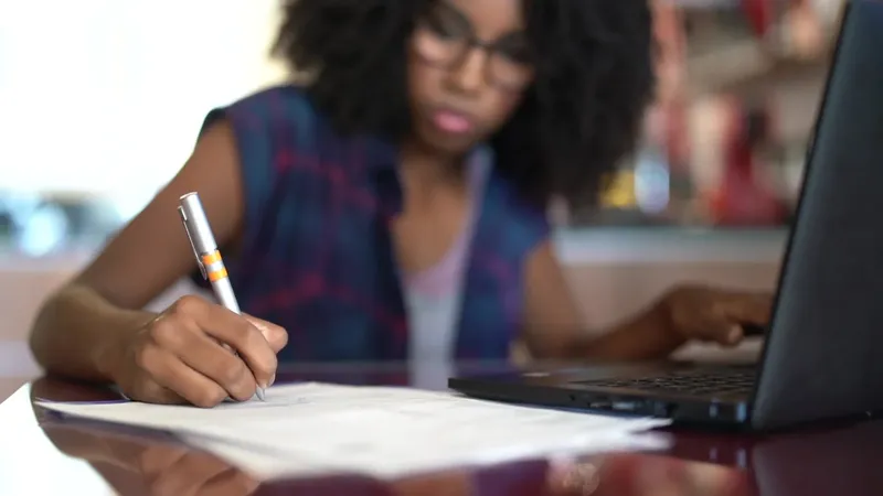 Jeune femme écrit sur un document avec un ordinateur portable
