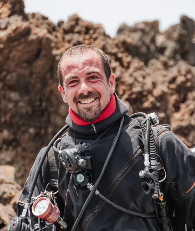 Plongeur souriant équipé de son matériel devant un fond rocheux