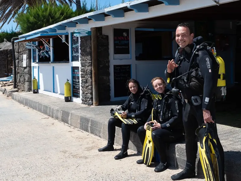 Trois plongeurs souriants équipés devant le centre de plongée