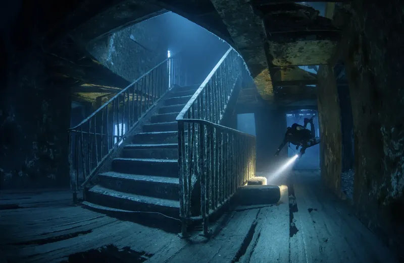 Plongeur explorant un escalier dans une épave sous-marine éclairée