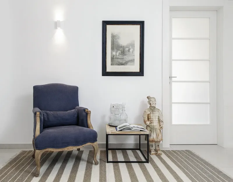 Intérieur lumineux avec fauteuil bleu, tableau, statue et porte vitrée