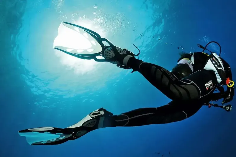 Plongeur en combinaison noire nageant dans une eau bleue claire