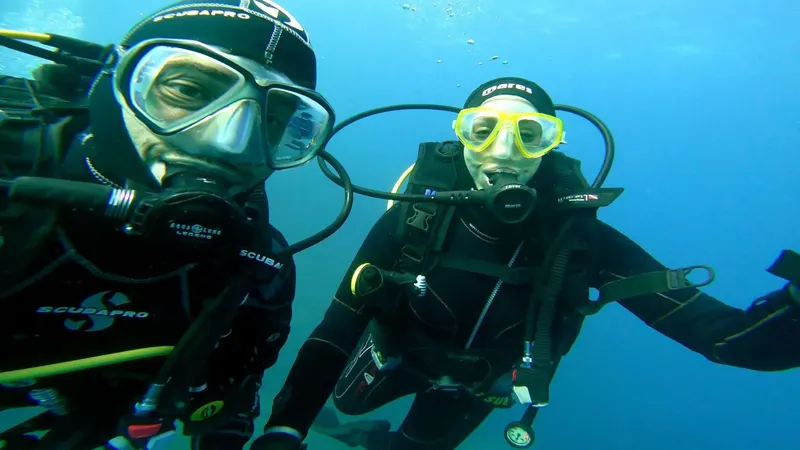 Deux plongeurs souriants avec leur équipement complet sous l'eau