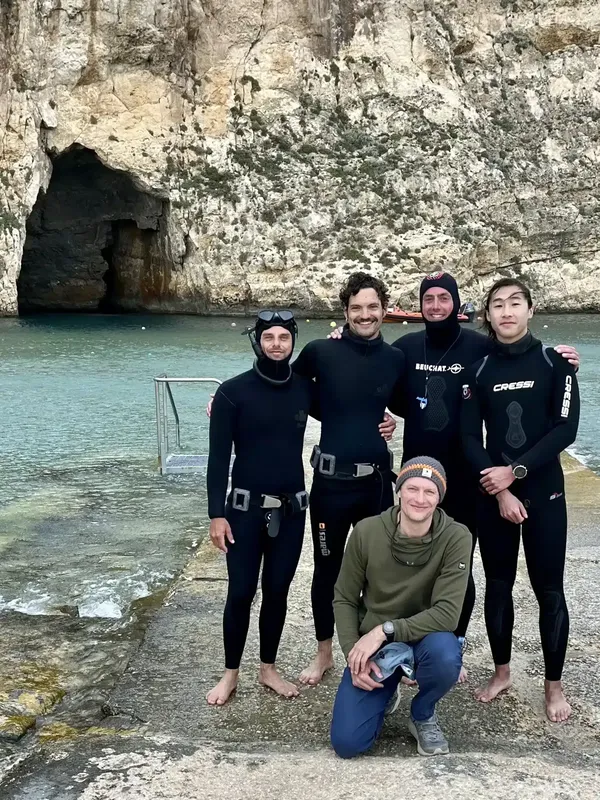 Quatre plongeurs souriants posent sur un quai rocheux en bord de mer