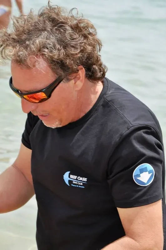 Homme portant des lunettes de soleil et un t-shirt noir sur une plage