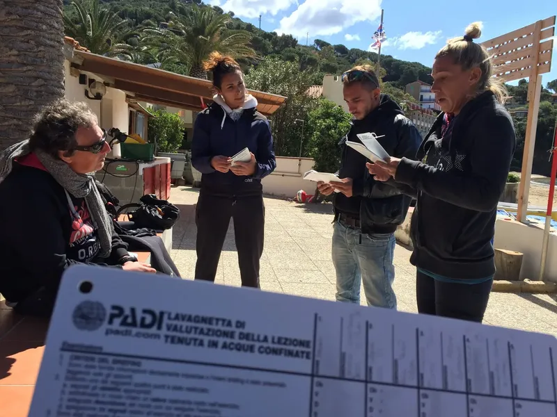 Quatre personnes discutent d'un document PADI en extérieur, combinaison de plongée