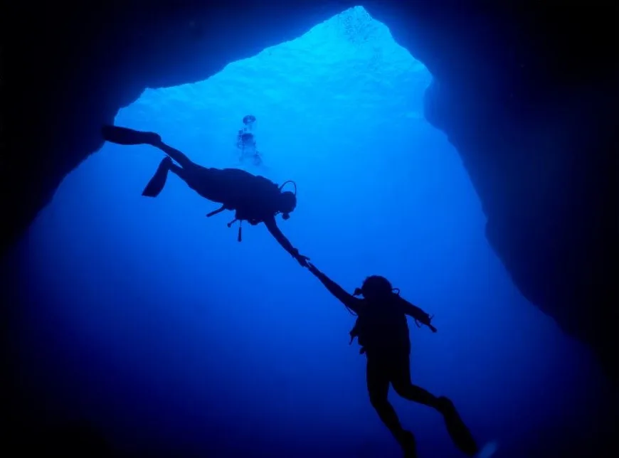 Deux plongeurs s'entraident dans une grotte sous-marine éclairée