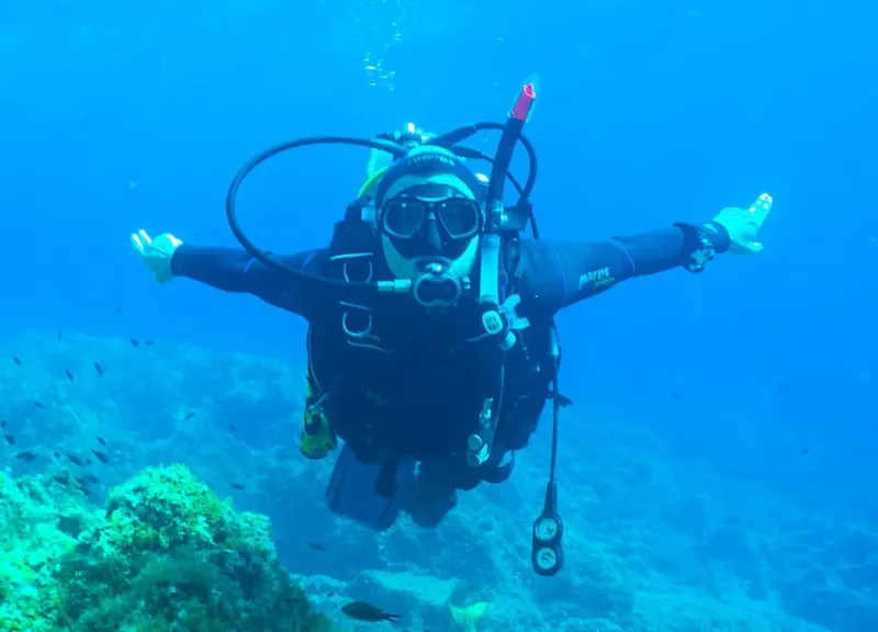 Plongeur en combinaison, bras ouverts, explore un récif sous-marin bleu