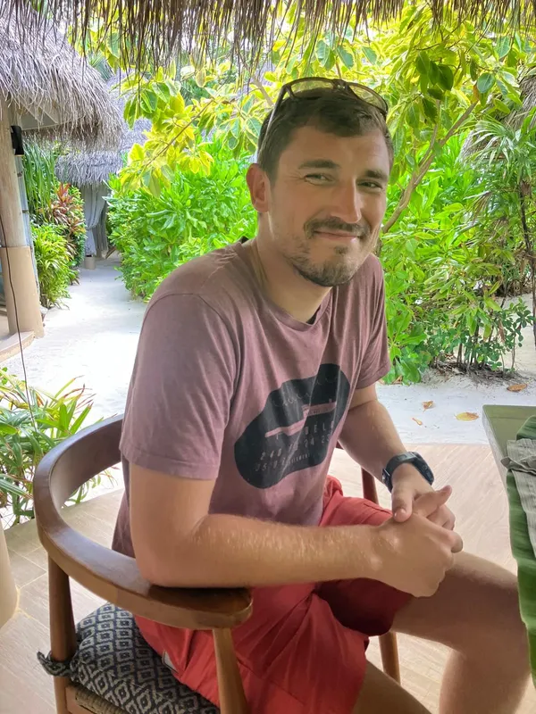 Un homme souriant est assis sur une chaise en extérieur