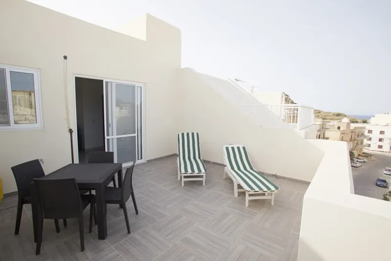 Terrasse avec table, chaises et transats, vue sur mer et bâtiments